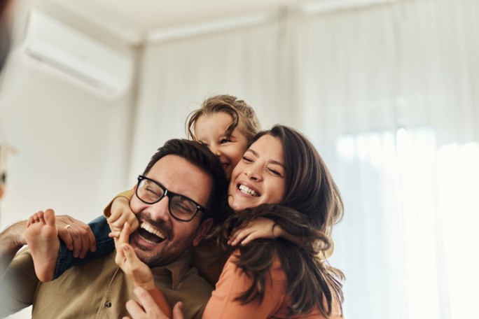 Happy little girl embracing her young parents at home. Copy space.
